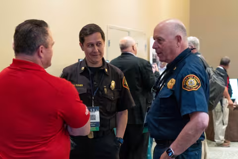 Two uniformed members of the fire service wearing 5x5 lanyards speak with another 5x5 attendee in the conference hall